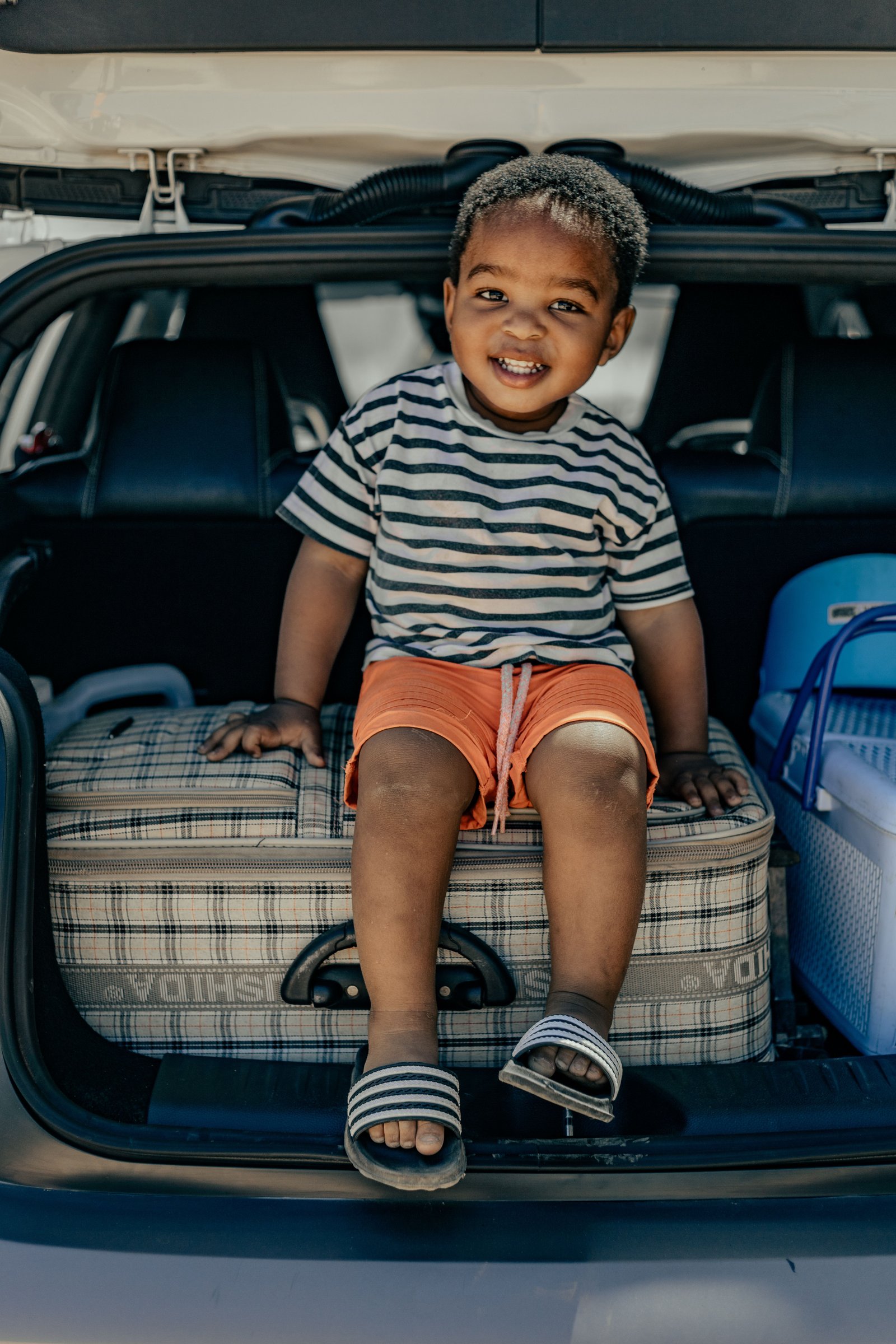 Tout-petit assis sur une valise dans le coffre familial avant le départ